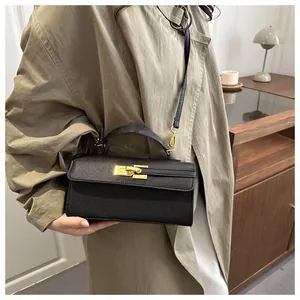 Détail du petit sac à main en cuir noir avec boucle dorée porté avec un trench-coat