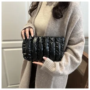Detailed close-up of a black quilted down clutch bag with vertical pleated texture