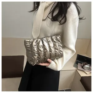 Detail of a champagne gold quilted puffy clutch bag held against a white sweater
