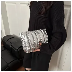 Detail of silver quilted puffer clutch bag held by model wearing black knit sweater