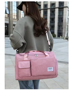 Pink corduroy duffel bag with shoulder strap shown in a city outdoor setting