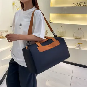 Deep blue travel bag with brown leather handles and orange shoulder strap on a model