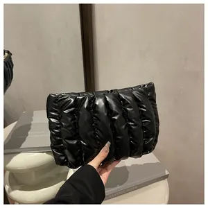 Detail view of a black quilted puffer clutch bag held by hand in a stylish setting