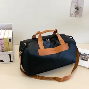 Close-up of black travel bag with brown leather handles and adjustable shoulder strap