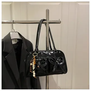 Detail of glossy black underarm bag featuring bow pockets and a tricolor wooden bead charm