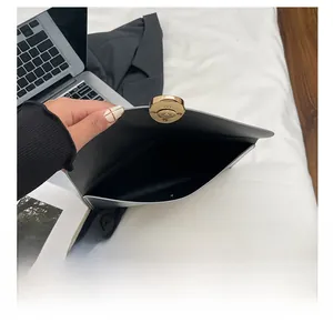 Detail of black leather envelope clutch featuring a gold magnetic button closure and spacious interior