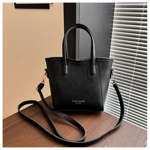 Detail of black pebbled leather tote with gold hardware and logo on wooden surface