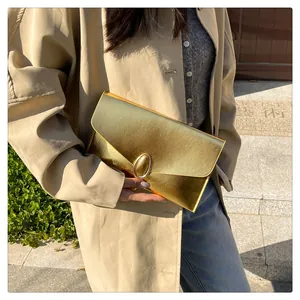 Chic gold envelope clutch bag with metal hardware and brushed texture worn outdoors