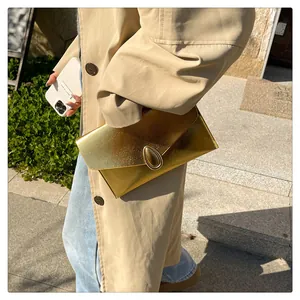 Detail of a textured gold envelope clutch bag featuring a teardrop metal clasp design