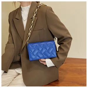 Detail of royal blue quilted handbag with chunky gold chain strap worn by a model