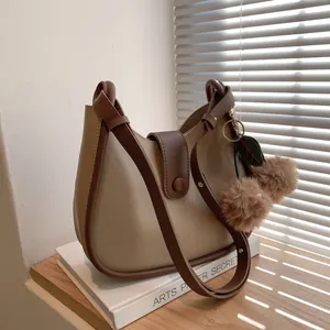 Chique beige schoudertas met bruine bies en pluche pompons op een houten vensterbank