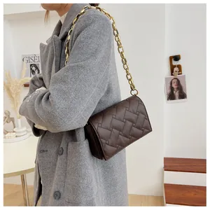 Detail shot of deep brown woven leather bag with a chunky gold chain strap on a model