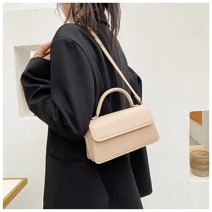 Détail d'un petit sac carré beige porté à l'épaule par un mannequin en blazer noir chic