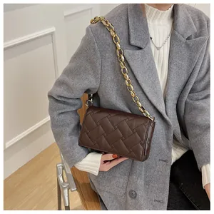 Detail of dark brown quilted crossbody bag with thick gold chain on model outfit