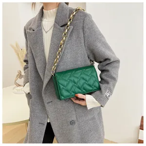 Detail of emerald green quilted crossbody bag with golden chain strap on a wool coat