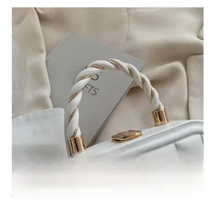 Detail of white evening bag with twisted gold metal and leather top handle texture
