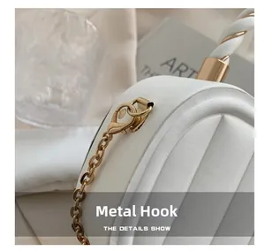 Detail of white quilted handbag showing golden metal chain hook and hardware clasp