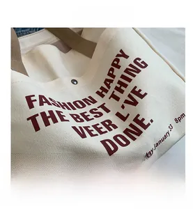 Detail shot of cream canvas tote bag with burgundy lettering and woven brown handles