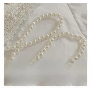 Detail showing glossy white pearl shoulder strap on soft lace fabric background