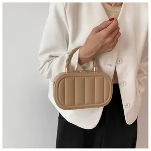Detail of beige quilted box bag with golden metal clasp and woven handle on model