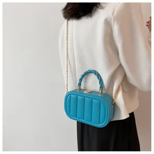 Detail of bright blue quilted handbag with gold chain strap and knot handle worn by model