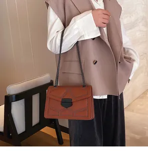 Détail du sac bandoulière en cuir fauve avec rivets sombres et chaîne sur mannequin