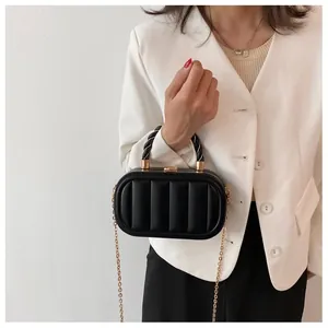 Detail view of a black quilted leather handbag with gold chain strap on white blazer