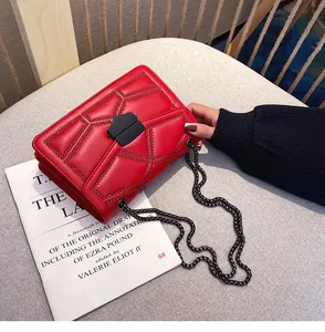 Détail du sac bandoulière en cuir rouge avec clous noirs et chaîne sur tissu gris