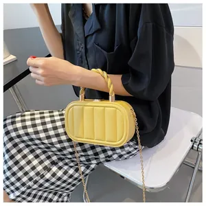 Detailed view of yellow quilted handbag featuring a braided handle and gold metal chain strap