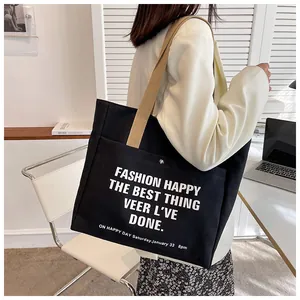 Close-up of black canvas tote bag with khaki handles worn by a model in a blazer