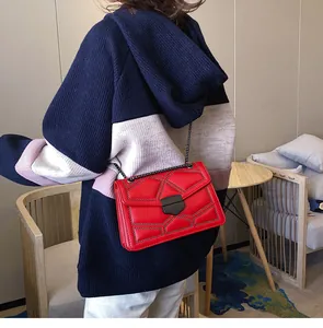 Détail du sac bandoulière rouge matelassé avec rivets métalliques et chaîne sur modèle