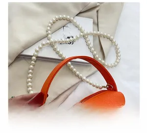 Détails d'un sac à main orange en cuir litchi avec une élégante anse en perles