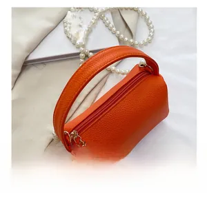 Gros plan d'un sac cylindre en cuir grainé orange avec chaîne de perles et fermeture