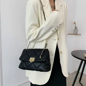 Elegant black quilted chain bag with gold buckle worn on white blazer crossbody style