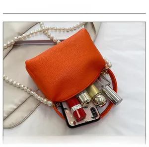 Vue de dessus d'un sac orange en cuir grainé montrant sa capacité et sa bandoulière perle