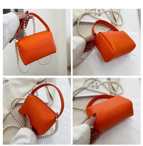 Détail du sac à main orange vif avec texture litchi, chaîne en perles et poignée
