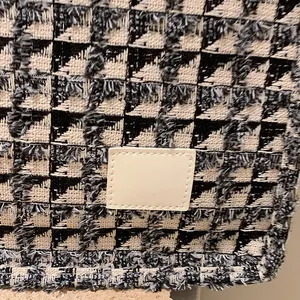Textured black and white checkered canvas tote bag with fringe detail and blank leather tag