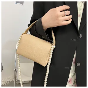 Sac seau en cuir grainé beige avec élégante bandoulière en perles porté par un mannequin