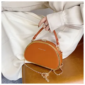 Detail van oranje maanvormige tas met gouden metalen frame en kettingriem