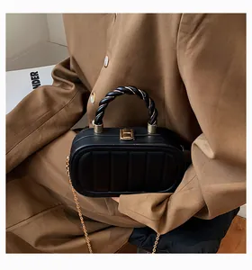 Detail of black quilted handbag with gold chain strap and woven top handle on brown blazer