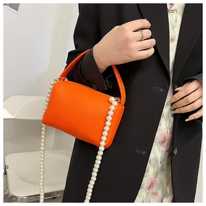 Gros plan du sac à main orange en cuir grainé avec bandoulière décorative en perles blanches