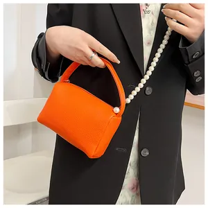 Détail du mini sac à main orange vif texturé litchi avec une élégante chaîne de perles
