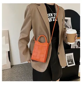 Orange woven leather mini handbag shown with a shoulder strap on a fashion model outfit