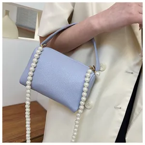Détail du sac en cuir lavande avec motif litchi, chaîne en perles blanches et zip doré