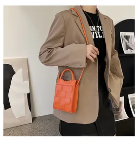 Close-up of bright orange woven mini handbag with crossbody strap on a beige blazer