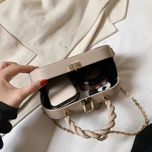 Minimalist beige crossbody bag with gold chain strap and textured handle on a fabric base