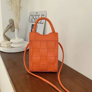 Vibrant orange woven crossbody handbag with top handle in an elegant lifestyle setting