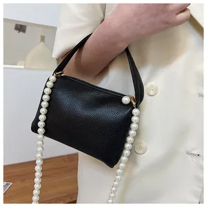 Détail d'un sac à main noir en cuir grainé avec une élégante chaîne en grosses perles