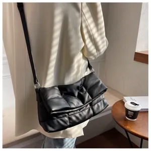 Detalle de bolso bandolera acolchado negro con hebillas plateadas sobre blazer crema