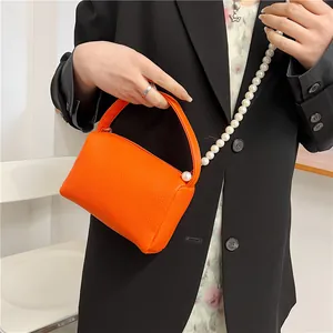 Sac à main orange vif en cuir grainé avec chaîne de perles porté par un modèle